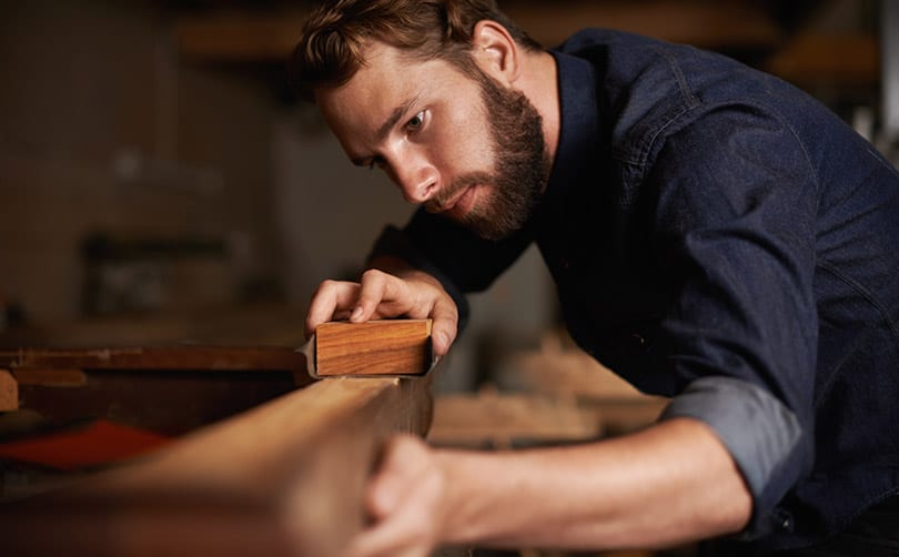 man with a beard hand sanding a fine piece of wood